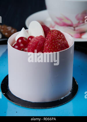 Il cioccolato bianco torta con fragole, lamponi e ribes servita su una piastra di colore blu Foto Stock