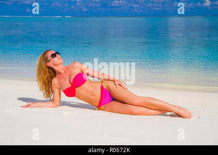 Ritratto di sorridente giovane donna posa sulla spiaggia e guardando lontano in rosa bikini e occhiali da sole. Spiaggia esotica con copia spazio, donne attraenti gode Foto Stock