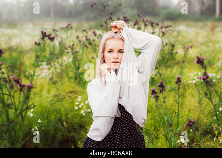 Ritratto di giovane ragazza danzante in campo di camomilla con le mani vicino al viso, thistle in primo piano Foto Stock