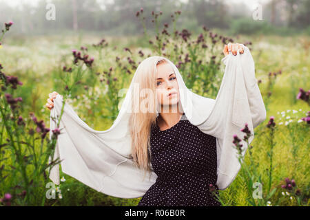 Ritratto di giovane ragazza danzante in campo di camomilla con mantello sulla testa, thistle in primo piano Foto Stock