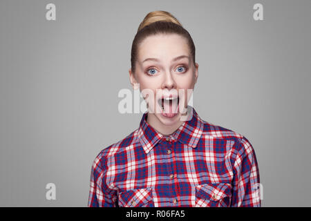 Ritratto di funny bella ragazza bionda in rosa Maglietta a scacchi, raccolti bun acconciatura e trucco in piedi con la bocca aperta e la lingua di fuori e grandi occhi. Foto Stock