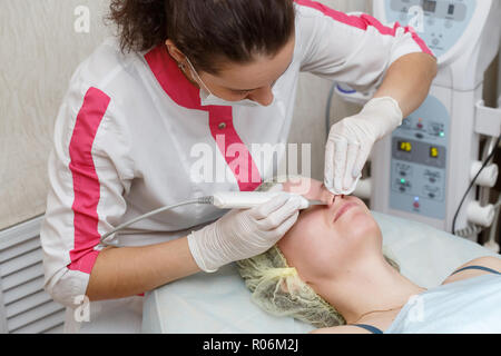 Cosmetologo eseguendo la procedura di pulizia viso con scrubber ad ultrasuoni in un salone di bellezza Foto Stock