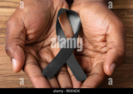 Persona della mano che tiene il nastro per supportare il melanoma della pelle la consapevolezza del cancro