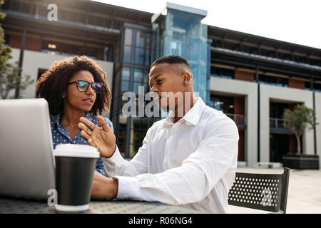 Giovane che parla di lavoro con colleghi. uomini d'affari che discutono di un nuovo progetto in ambienti esterni con notebook. Foto Stock
