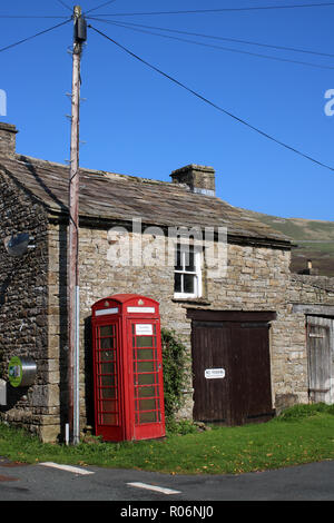 Iconico telefono rosso nella casella di fronte all edificio tradizionale in pietra in Thwaite, un piccolo villaggio nel Swaledale, Yorkshire Dales, North Yorkshire, Inghilterra, Regno Unito Foto Stock