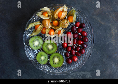 Physalis frutta - Ribes del Capo con mirtilli e kiwi su taglio piatto di vetro su sfondo di ardesia - centrato Foto Stock