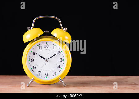 Giallo antico orologio retrò sulla scrivania in legno e sfondo nero. Orologio con il campanello di allarme. Spazio per testo e design. Concetto di tempo Foto Stock