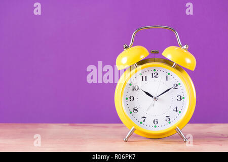 Allarme vecchio orologio retrò con campana sulla scrivania in legno e sfondo viola. Orologio è in colore giallo. Spazio per testo e design. Tempo Concetto di immagine Foto Stock