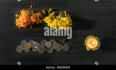 Accesa diya e monete poste su sfondo nero per celebrare Diwali e Dhanteras Foto Stock