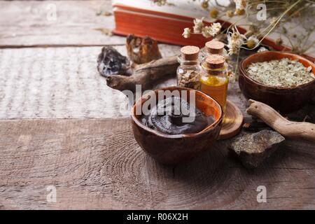 Preparazione cosmetica fango nero maschera nel recipiente di ceramica su vintage sfondo di legno. Vista frontale del viso emulsione di argilla sulla tabella con i prodotti spa. Natura Foto Stock