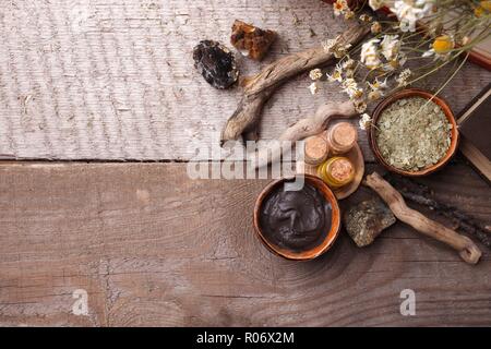 Preparazione cosmetica fango nero maschera nel recipiente di ceramica su vintage sfondo di legno. Vista superiore del viso emulsione di argilla sulla tabella con i prodotti spa. Natural Foto Stock