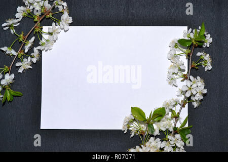 Cornice di fiori bianchi intorno a un foglio di carta su uno sfondo nero. Foto Stock