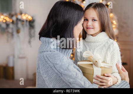 Giovani femmine abbraccia il suo bambino, dà presente, si congratula con il nuovo anno, orgogliosi di avere così belli e figlia intelligente. Capretto felice spende Foto Stock