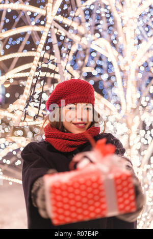 Giovane ragazza in piedi di fronte ad albero di natale luci nasconde dietro presenta da sola nel parco, defocalizzazione sul presenta Foto Stock