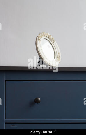 Fronte verticale visualizza i dettagli di White round picture frame su blue vintage cassa di legno di cassetti con maniglie nere contro la parete di luce naturale copys Foto Stock