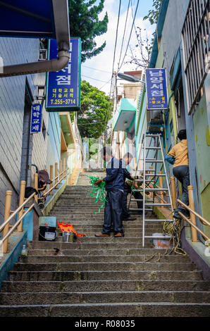 Operai saldo una scaletta su una lunga rampa di scale da fare alcuni lavori di manutenzione su una proprietà in Busan, Corea del Sud. Foto Stock