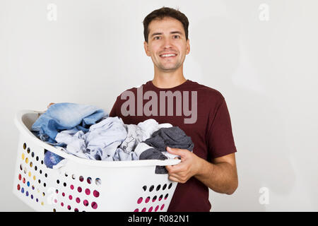 Giovane con sorriso holding cesto pieno di vestiti. Lavori di casa dopo il lavoro Foto Stock