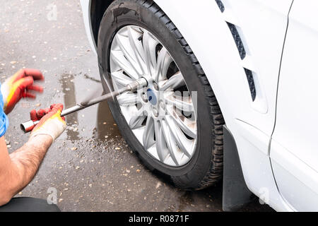 Il tecnico si svita auto ruota mediante la chiave di manovra all'aperto stagionale per la sostituzione dei pneumatici Foto Stock