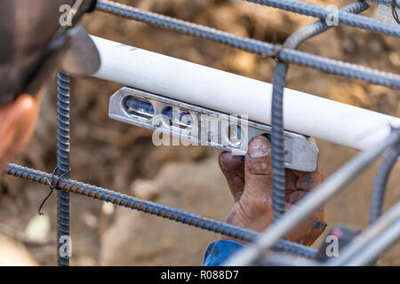Plumber utilizza il livello mentre si installa il tubo in PVC al sito in costruzione. Foto Stock