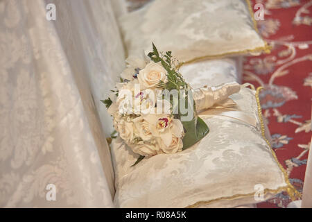 La doppia bouquet in appoggio sui cuscini bianchi del banco di nozze dentro la chiesa dove la celebrazione si è tenuta. Foto Stock