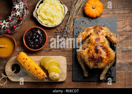 Elevato angolo di visione di un tacchino arrosto posto su una tavola in legno rustico accanto ad alcune ciotole con salsa, purè di patate, confettura di mirtilli, alcune fette di roaste Foto Stock