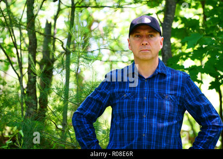 Un grave caucasica l uomo sta cercando la telecamera per un ritratto durante le escursioni nella foresta che indossa un controllo blu T-shirt e un cappello nero. Foto Stock