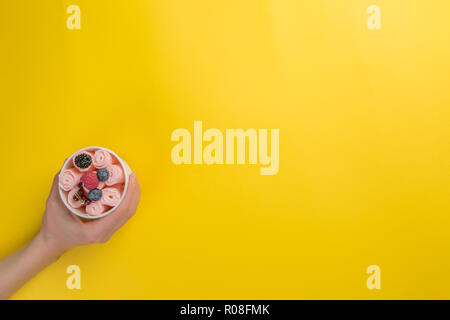 Mani tenendo le tazze con laminati diversi gelati su colore giallo brillante background, vista dall'alto Foto Stock