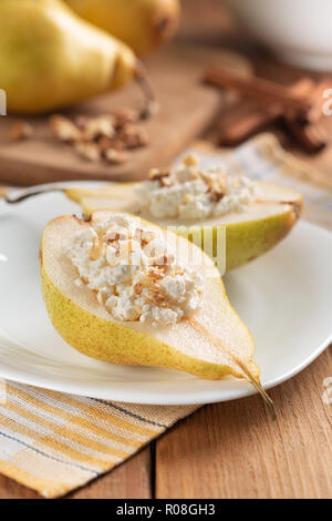 La metà delle pere con ricotta e i dadi sul piatto bianco. Tavolo in legno, sfondo sfocato. Concetto - cibo sano e salutare prima colazione. Close-up. Foto Stock