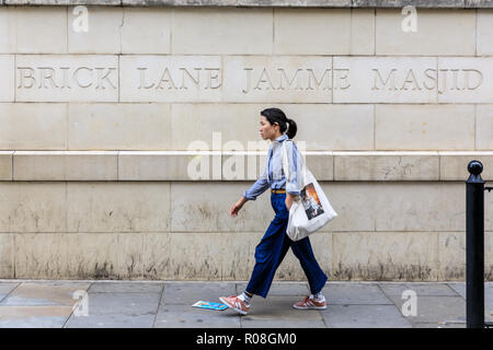 Una donna cammina passato Brick Lane Jamme Masjid, Brick Lane moschea nella zona est di Londra, Regno Unito Foto Stock