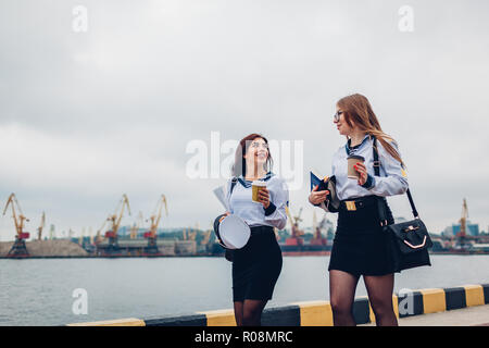 Due college studenti donne di Marine Academy a piedi dal mare indossando uniforme. Amici camminare, parlare e puntamento in distanza Foto Stock