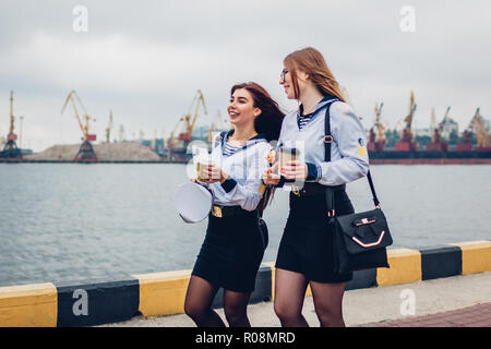 Due college studenti donne di Marine Academy a piedi dal mare indossando uniforme. Amici camminare, parlare e puntamento in distanza Foto Stock