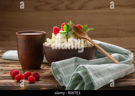 Per la ricotta con il cucchiaio di legno su di esso e il latte in clayware sul tavolo di legno Foto Stock