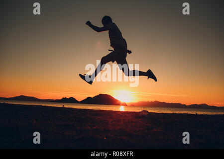 Giovani energico uomo felice jumping in riva al mare Foto Stock