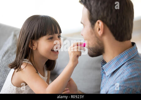 Figlia divertente tenere il rossetto applicare cosmetici sul padre labbra Foto Stock