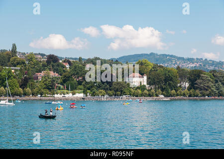 Vista sul lungomare di Ouchy area nella città di Losanna, Svizzera con piccole barche sul lago Lemano (Lago di Ginevra) sulla soleggiata giornata estiva con cielo blu e nuvole Foto Stock