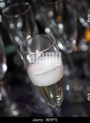 Bicchiere di vino spumante appena versata con un frizzante di testa. Offuscata, sfondo bokeh di fondo Foto Stock