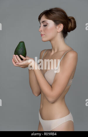 Varie espressione da ragazza giovane con avocado frutta fresca su sfondo neutro Foto Stock