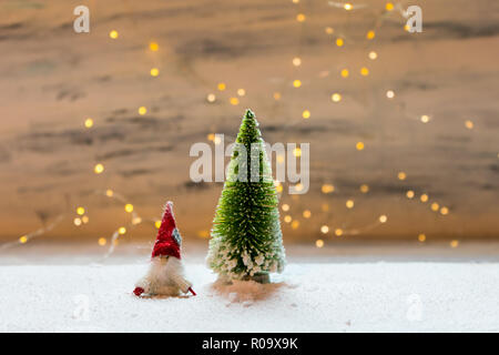 Sybolic paesaggio con natura concettuale, un unico verde albero di Natale e un po' di Santa Claus in piedi nella neve su uno sfondo di luci Foto Stock