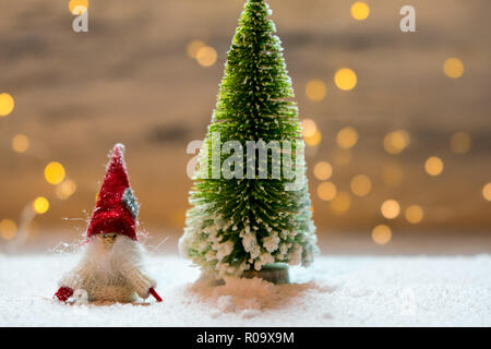 Sybolic paesaggio con natura concettuale, un unico verde albero di Natale e un po' di Santa Claus in piedi nella neve su uno sfondo di luci Foto Stock