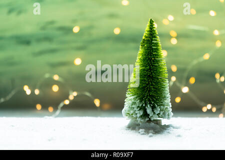 Sybolic paesaggio con natura concettuale, un unico verde albero di Natale in piedi nella neve su uno sfondo di luci bianche Foto Stock