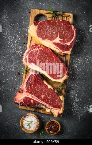 Carne cruda carne di manzo. Il Black Angus primo set di carne - bistecca di controfiletto, t-bone bistecche sul bordo di taglio. Vista dall'alto sulla tavola nera. Foto Stock