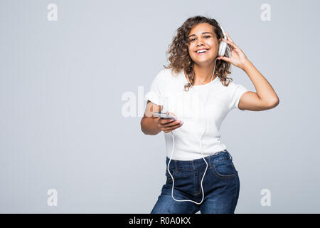 Gioiosa donna latinoamericana in abbigliamento casual per ballare e ascoltare musica con piacere tramite gli auricolari bianco isolato su bianco Foto Stock