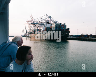 Il vecchio uomo e donna giovane guardando al di fuori di un traghetto a un contenitore di carico della nave Foto Stock