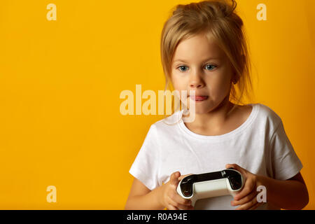 Poco assorbiti ragazza in t-shirt bianco tenendo un game pad la riproduzione del video gioco su sfondo giallo Foto Stock