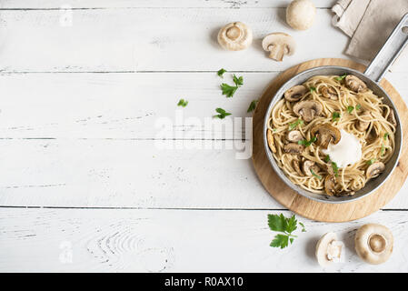 Fungo Spaghetti e salsa alla panna su sfondo bianco, vista dall'alto. In casa la pasta italiana con funghi champignon in padella di cottura. Foto Stock