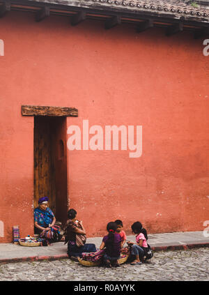 La matriarca della famiglia guatemalteco nel tradizionale abito Maya vende gioielli e panni di cesti sulla strada vicino alla sua famiglia in Antigua Guatemala Foto Stock