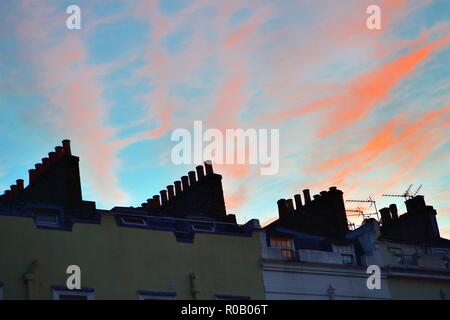 Londra, Inghilterra, Regno Unito. Poco prima del tramonto, la finale di sole del giorno imposta il wispy nuvole sul fuoco sopra i camini tradizionali. Foto Stock