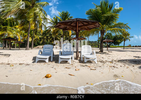 Concetto di vacanza - tre sedie di legno e Palapa tetto sole ombrellone sulla spiaggia tropicale - l'isola caraibica di Guadalupa Foto Stock