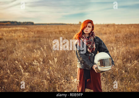 Giovane ragazza redhead in nero giacca di pelle e casco di volo all'aperto Foto Stock