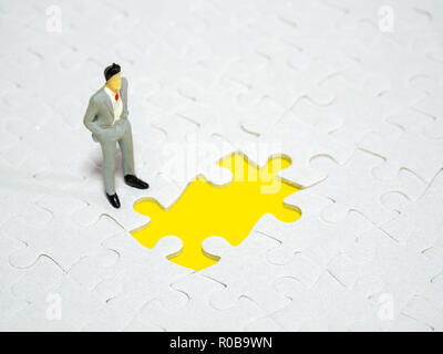 Imprenditore in piedi nella parte anteriore del pezzo mancante jigsaw su sfondo giallo. Foto Stock